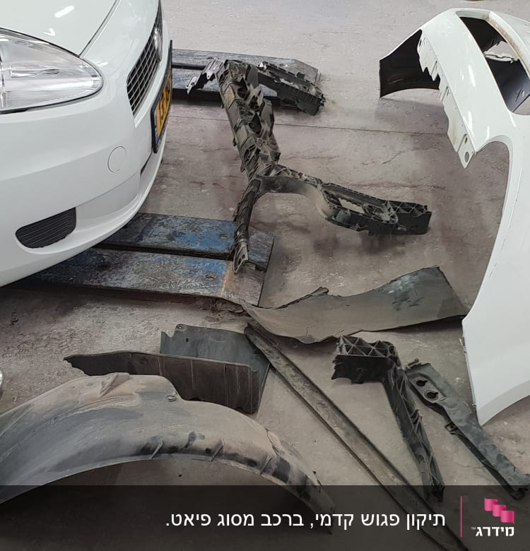 חלקי רכב מפורקים ליד רכב לבן במוסך